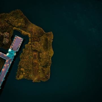 An aerial shot of a dock on the body of the ocean surrounded by an island of trees