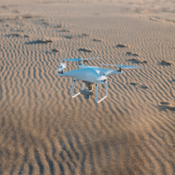 High end technology flying drone landing on sand at beach or desert during beautiful sunset or sunrise light. Tool for aerial footage for photographers and social media content creators