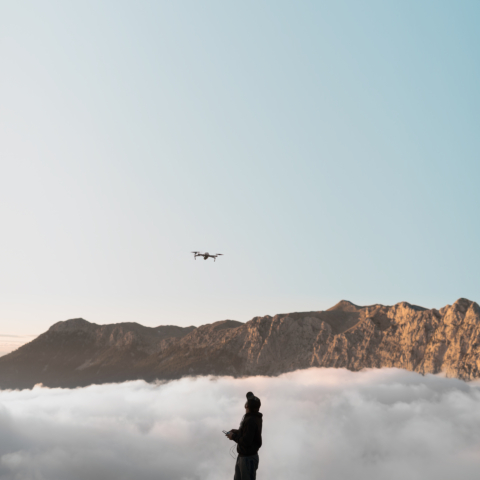 Man outdoors with remote control flying a drone in the mountains with sky on horison