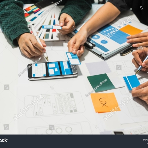 stock-photo-a-group-of-people-collaborates-around-a-desk-discussing-and-reviewing-user-interface-ui-and-user-2492369847