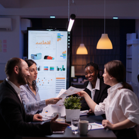 Workaholics businesspeople brainstorming financial company ideas analyzing strategy paperwork late at night in business office meeting room. Multi-ethnic coworkers checking solution