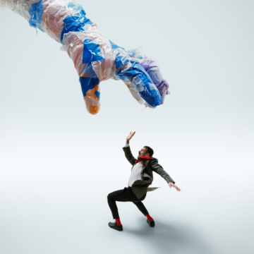 Young caucasian man avoiding big plastic hand on white studio background. Male model in office attire fighting in motion and action. Looks angry, scared, pressured. Eco problems, pollution, recycling.